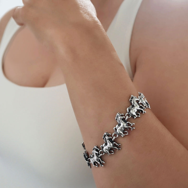Silver bracelet with horse links on a woman's wrist against a neutral background