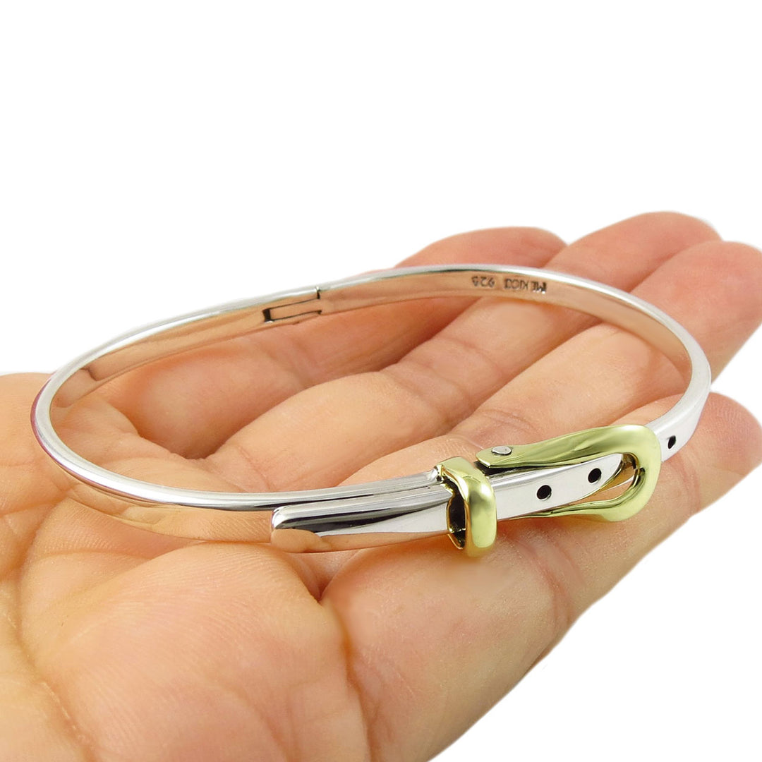 Silver buckle bracelet with a gold clasp held in a hand on a white background