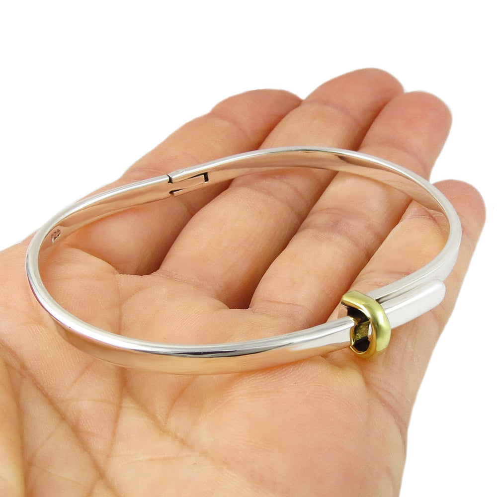 Silver bangle with a gold accent on a hand against a white background