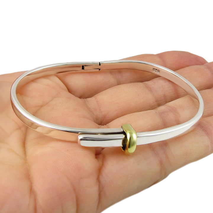 Silver and gold bangle on a hand against a white background