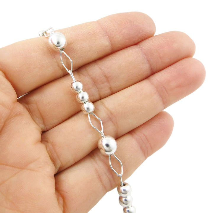 An unusual wide link UK hallmarked 925 sterling silver chain bracelet decorated with polished ball beads and held in a person's hand on a white background. 