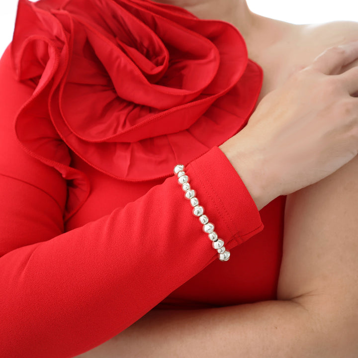 A woman wearing a red dress with a large floral design and a UK hallmarked shiny 925 sterling silver beaded bracelet.