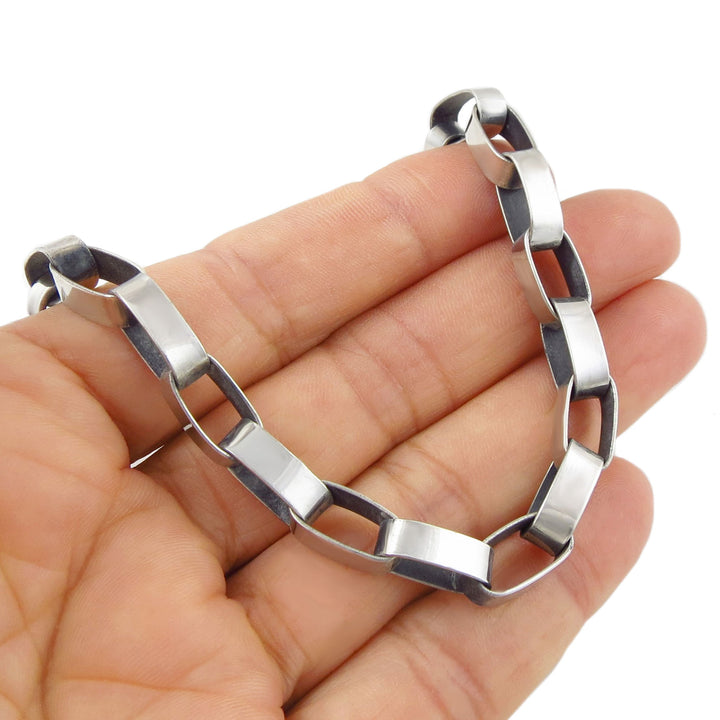 Large ovaal link brutalist chain bracelet in sterling silver held in a person's hand on a white background. 