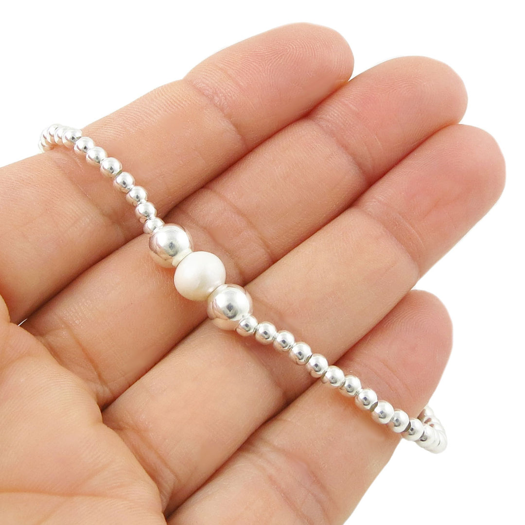 925 sterling Silver beaded bracelet with a white pearl held between fingers on a white background