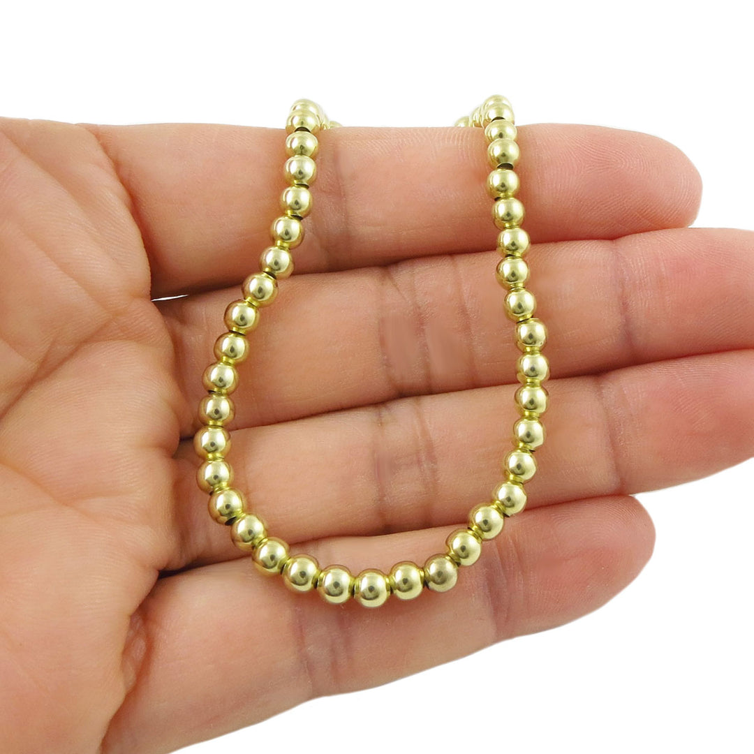 A stretch bracelet featuring gold beads on a hand against a white background