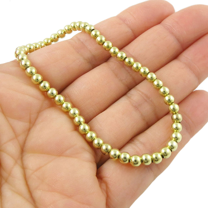 Gold beaded bracelet on a hand against a white background