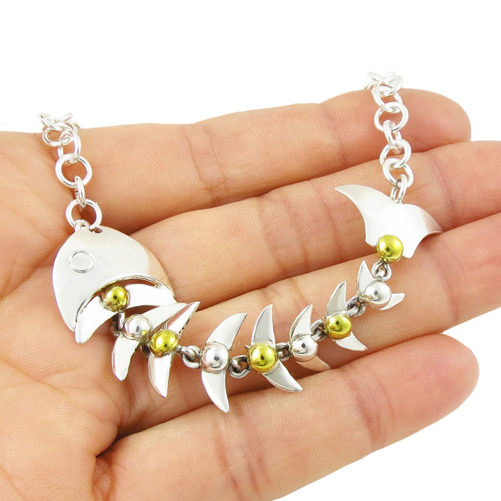 A large sterling 925 silver and gold Taxco fish skeleton bracelet held in a person's hand on a hite background. 