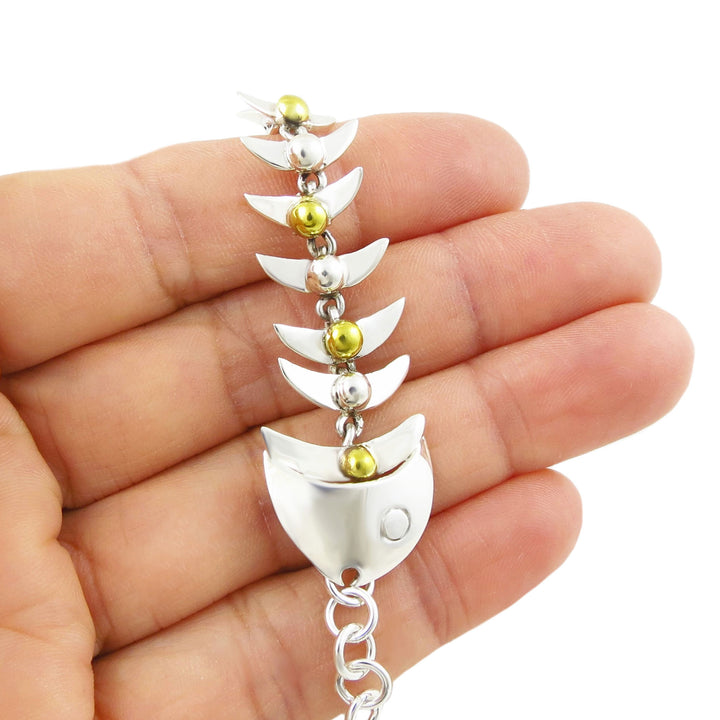 925 sterling silver and gold beaded fish skeleton and chain bracelet held between fingers on a white background