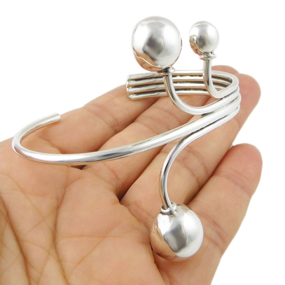 Ladies statement sterlling 925 silver cuff style bracelet with spherical ends held in a hand against a white background