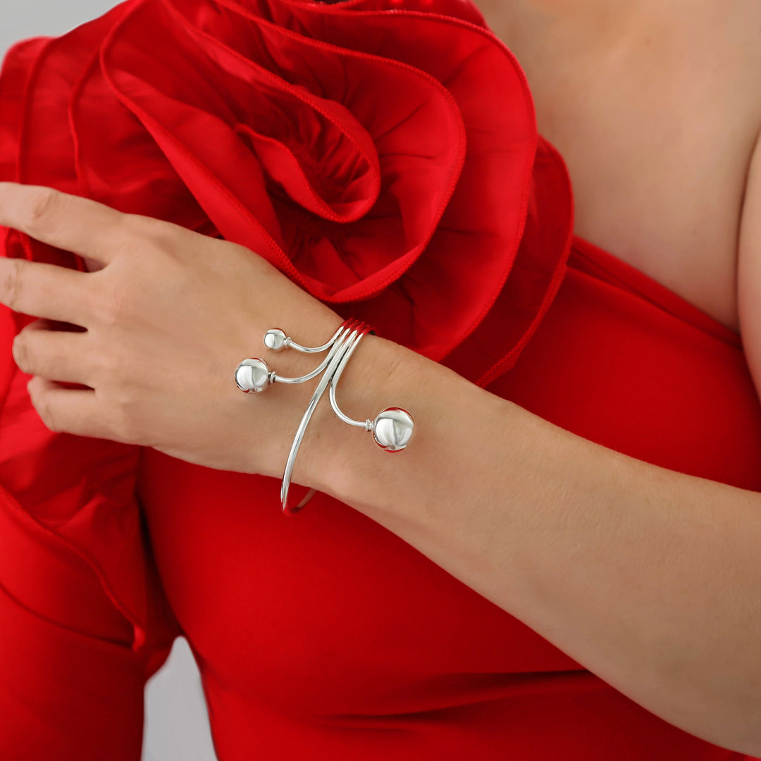 A woman in a red dress with a frill wearing a large statement silver bracelet cuff on one wrist. 