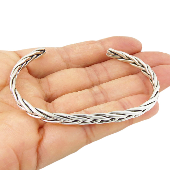 A solid 925 sterling silver braided cuff bracelet held in a person's hand