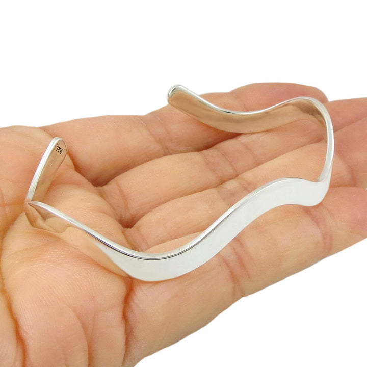 Sterlling 925 silver wave cuff bracelet with a polished finish on a hand against a white background