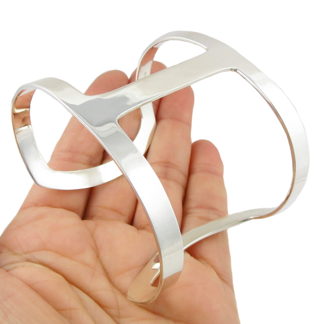 a wide handmade sterling silver sculpted bracelet UK hallmark held in a hand on a white background