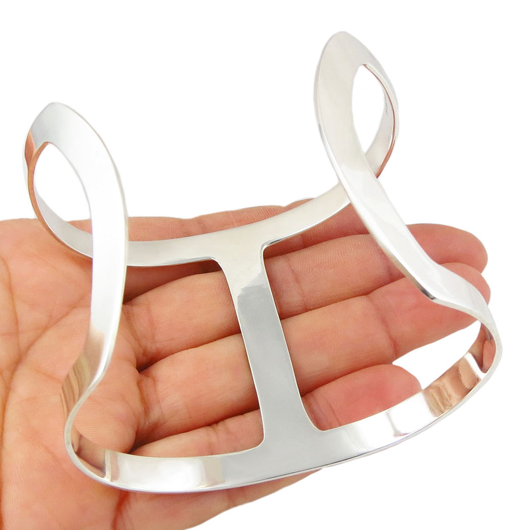 The reverse of a wide statement handmade cuff style braceket with UK hallmark held in a person's hand. 