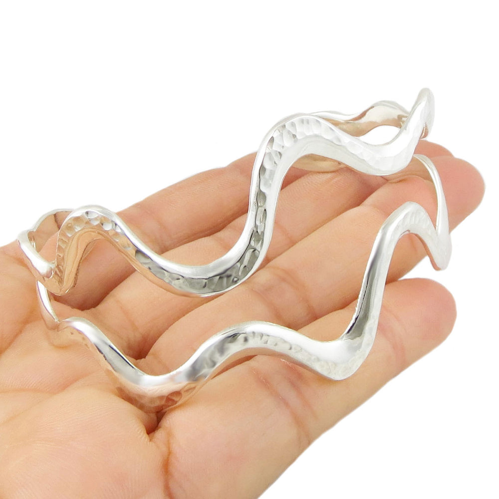 Silver wave-shaped handmade UK bracelet cuff held in a hand on a white background