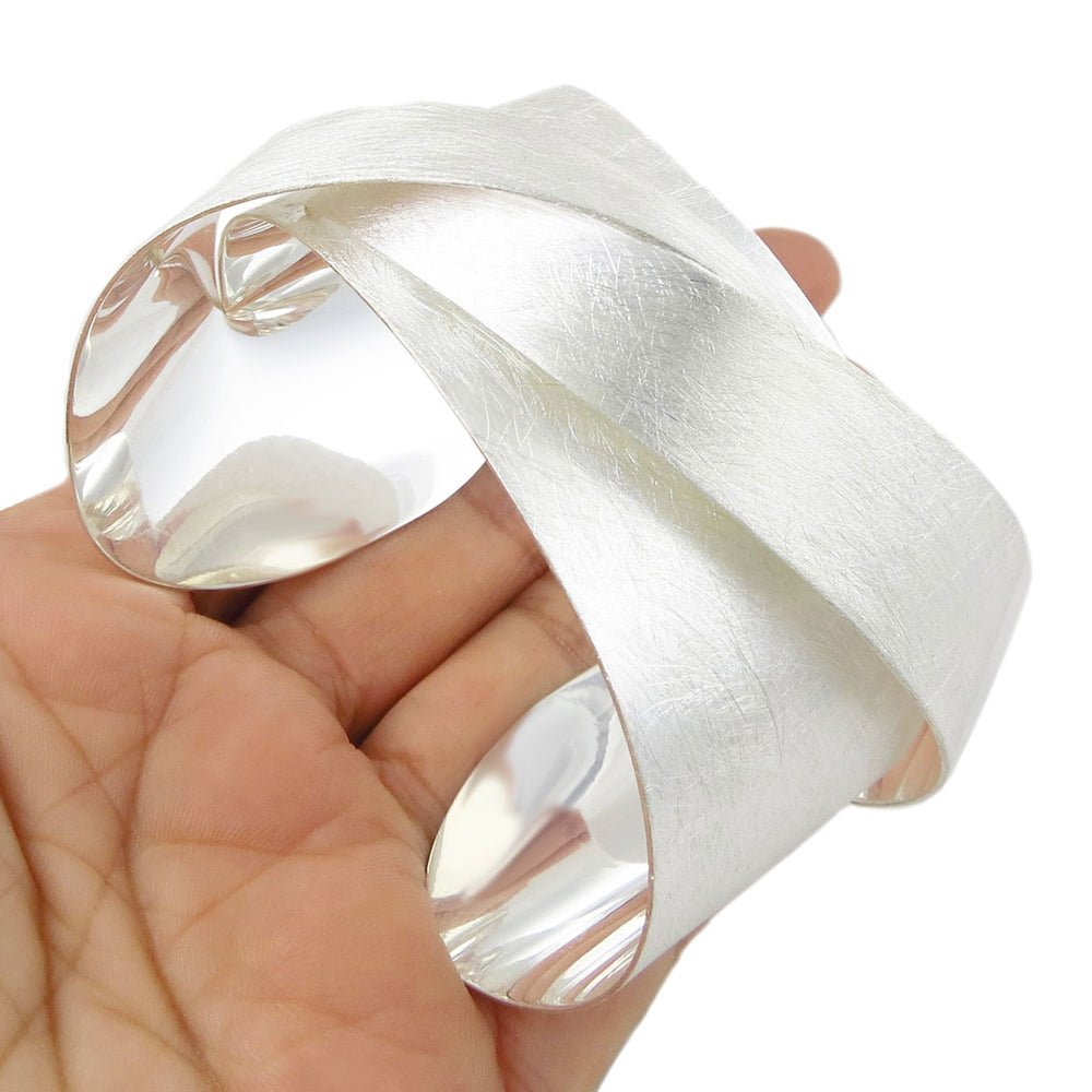 Large silver bracelet with a matt brushed finish being held in a hand on a white background