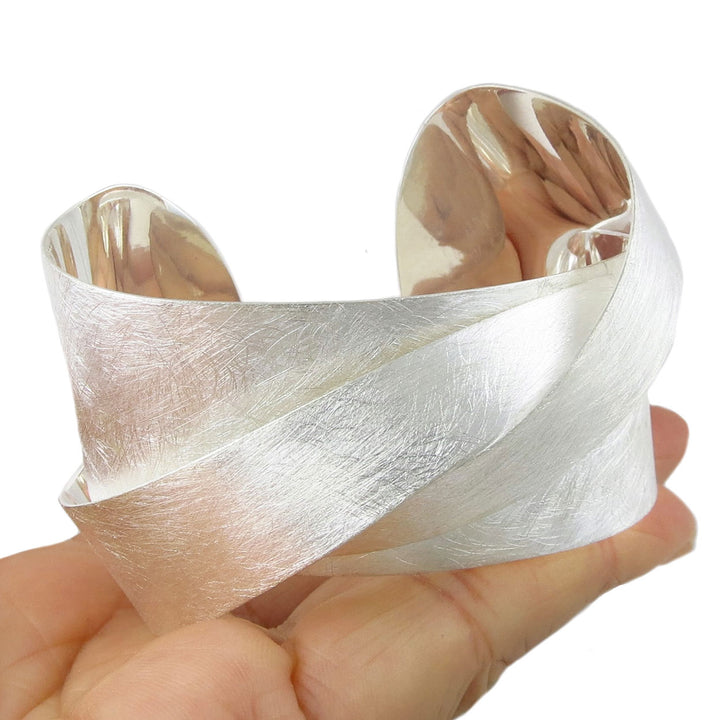 Silver cuff bracelet with a brushed finish held in a hand on a white background