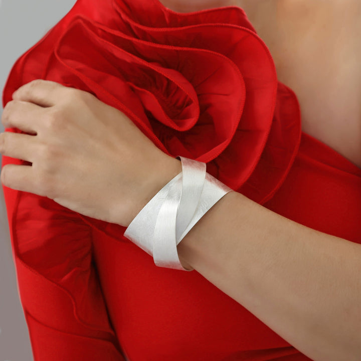 Woman in a red dress wearing a large silver bracelet with a matt brushed finish. 