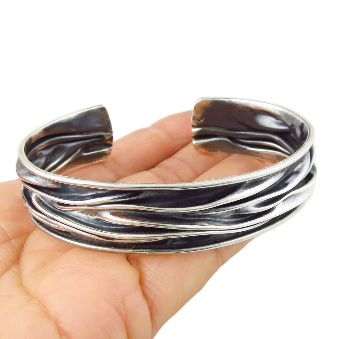 Silver cuff bracelet handmade UK with a crumpled finish on a hand against a white background