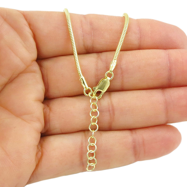 Gold snake chain bracelet with a lobster claw clasp and an extension chain to adjust the length held in a hand on a white background