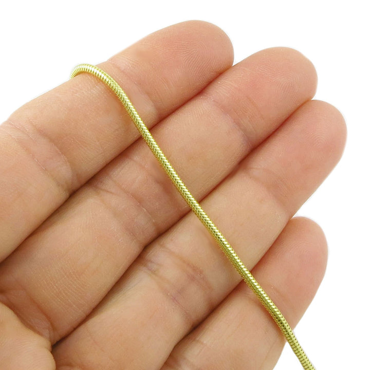 14ct yellow gold snake chain bracelet held between fingers on a white background