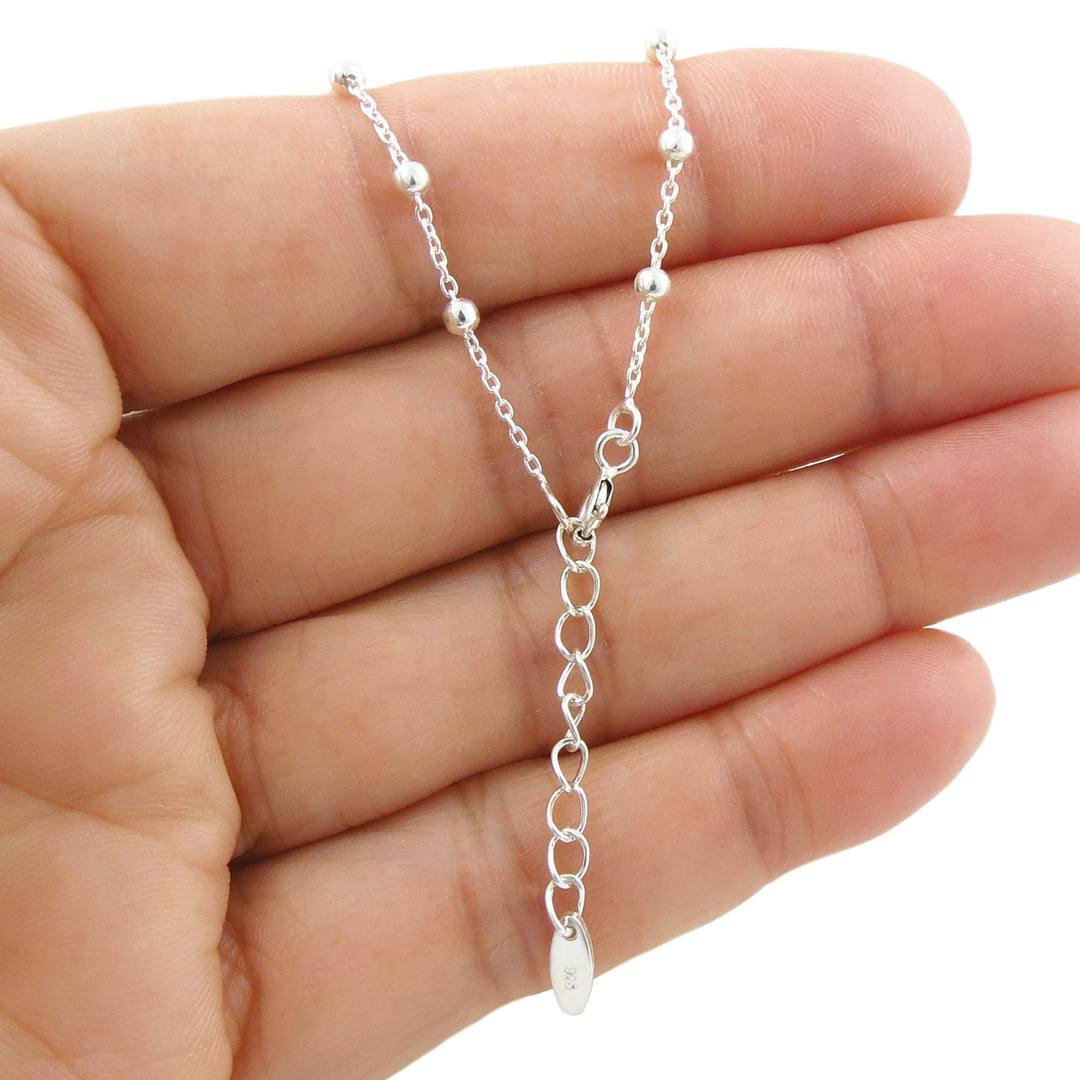 A silver chain bracelet eith a lobster claw fastener and an extension chain held in a person's hand against a white background