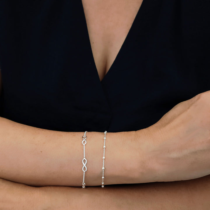 Woman wearing a 925 sterling silver bracelet stack featuring a figure of eight chain and a beaded chain against a black background