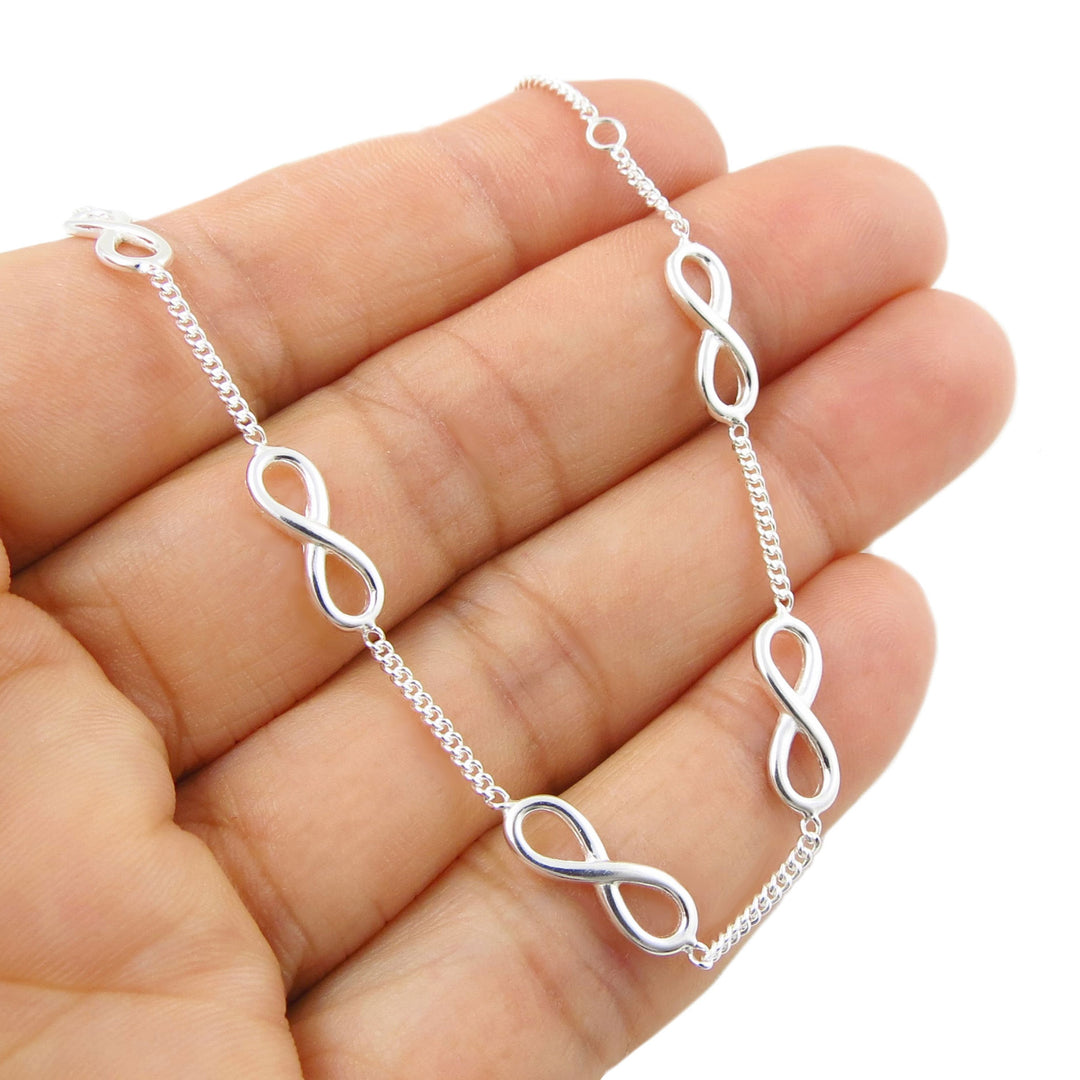 A sterling silver cub chain figure of eight stacking bracelet held in a person's hand on a white background