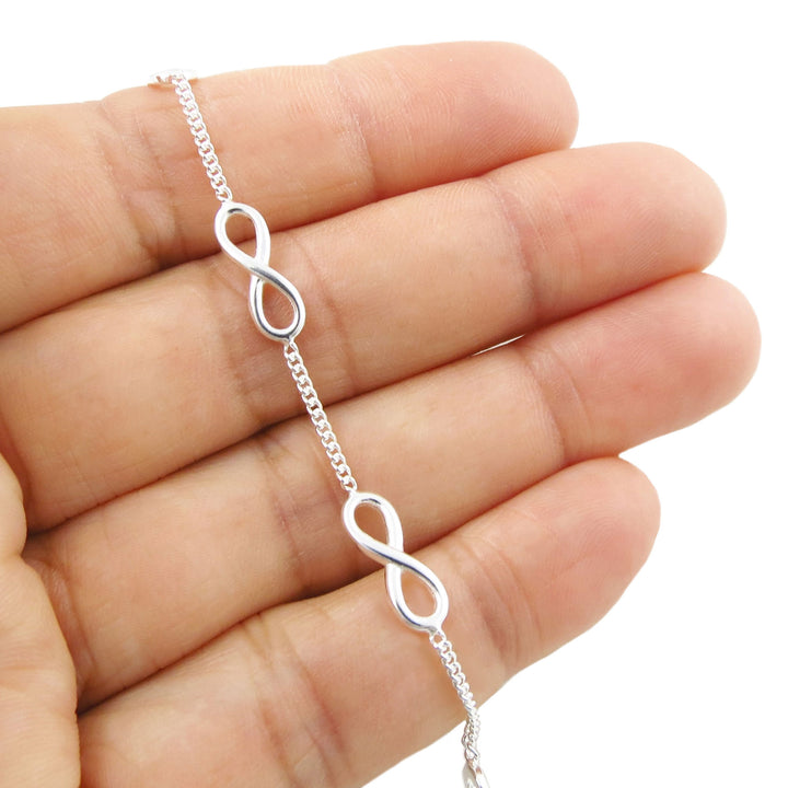 Silver curb chain bracelet with infinity symbol links on a hand against a white background
