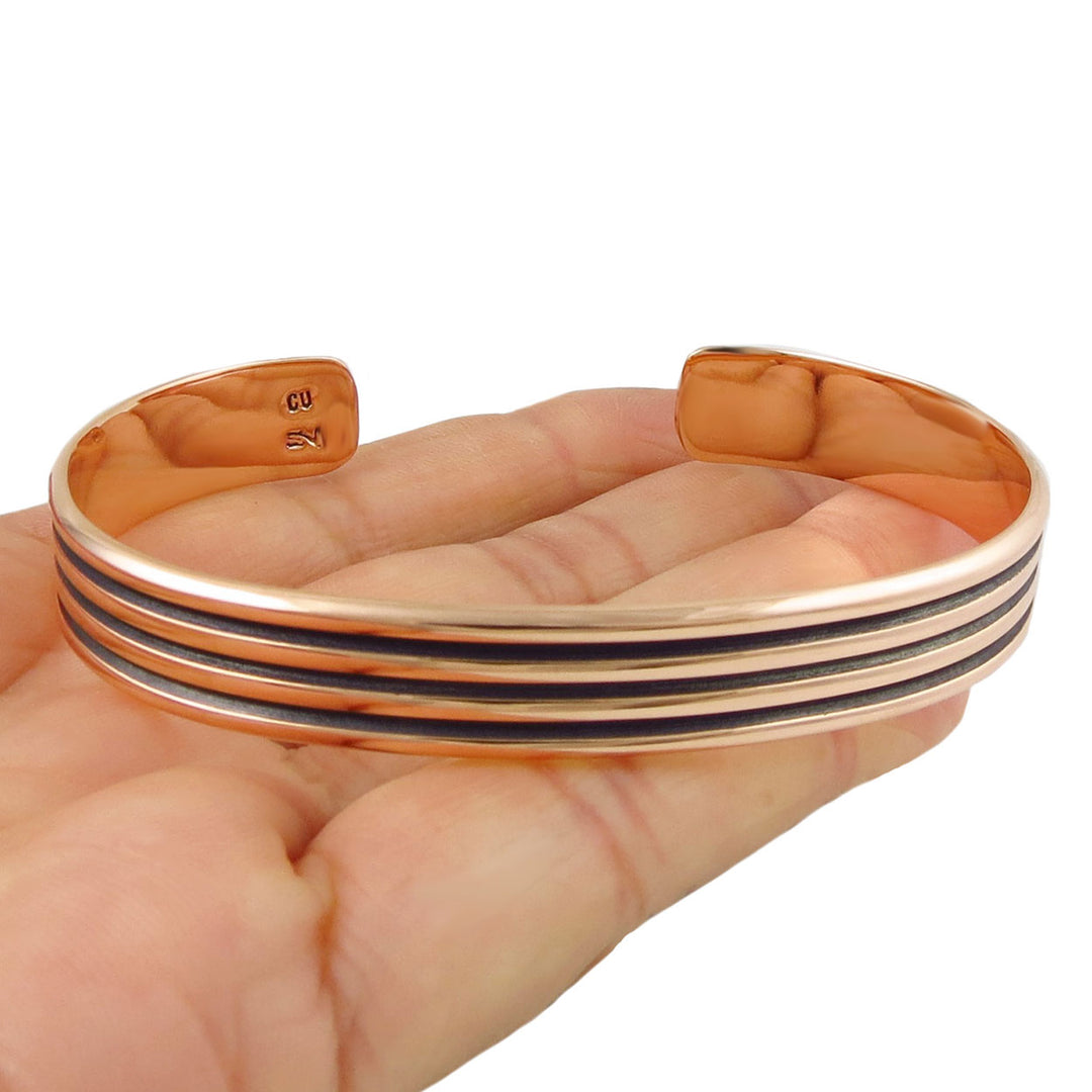 Solid copper ladies bracelet with three lines held in a hand on a white background