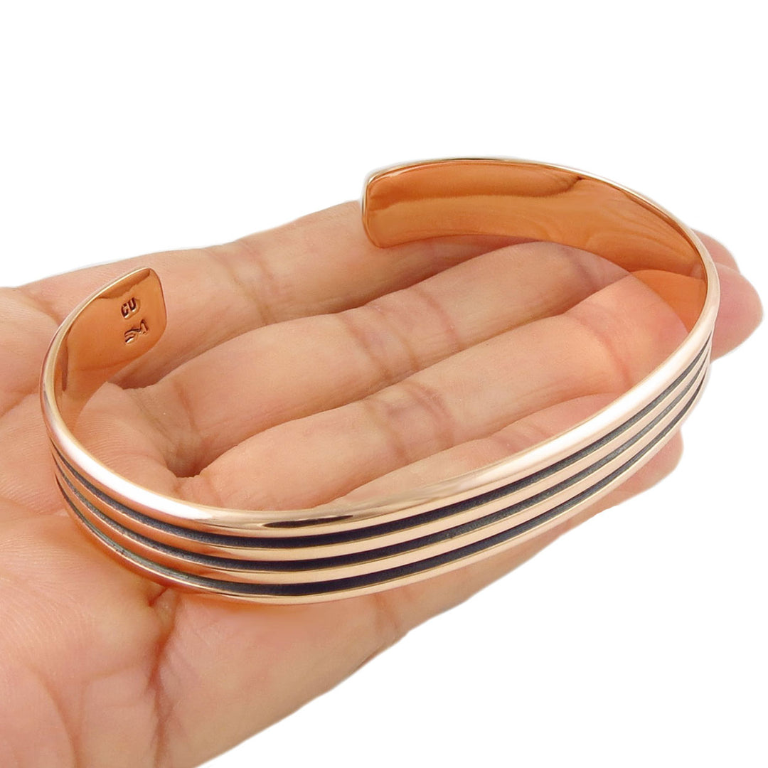 Solid copper bracelet decorated with three stripes on a hand against a white background