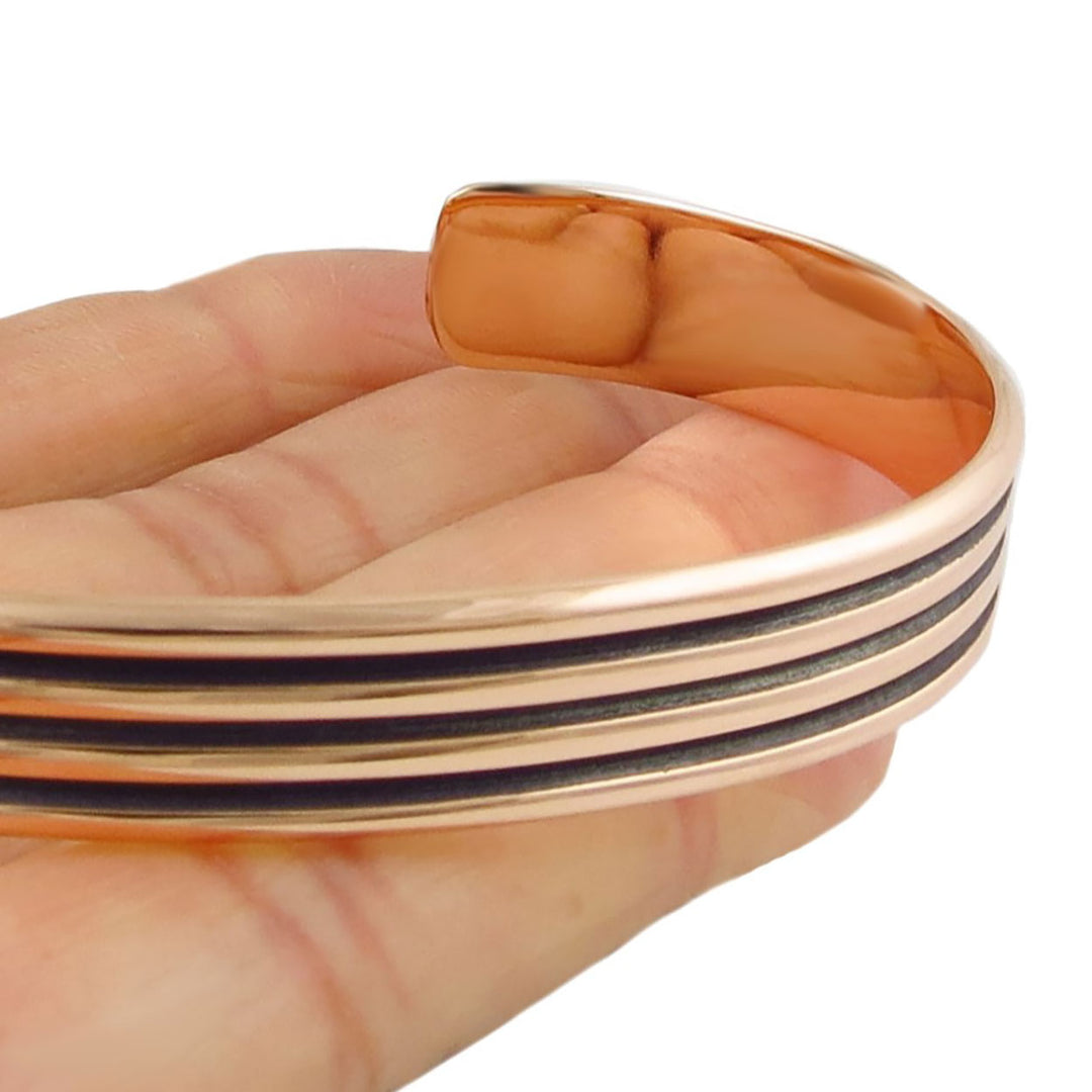 Women's copper bracelet with black grooved lines on a hand against a white background