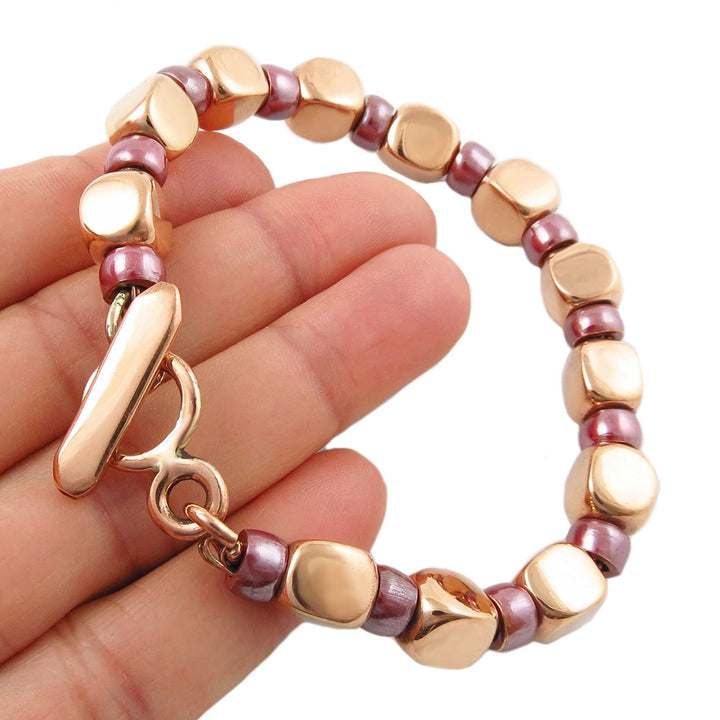 Bracelet with polished square copper and pink  beads held by a woman's hand on a white background
