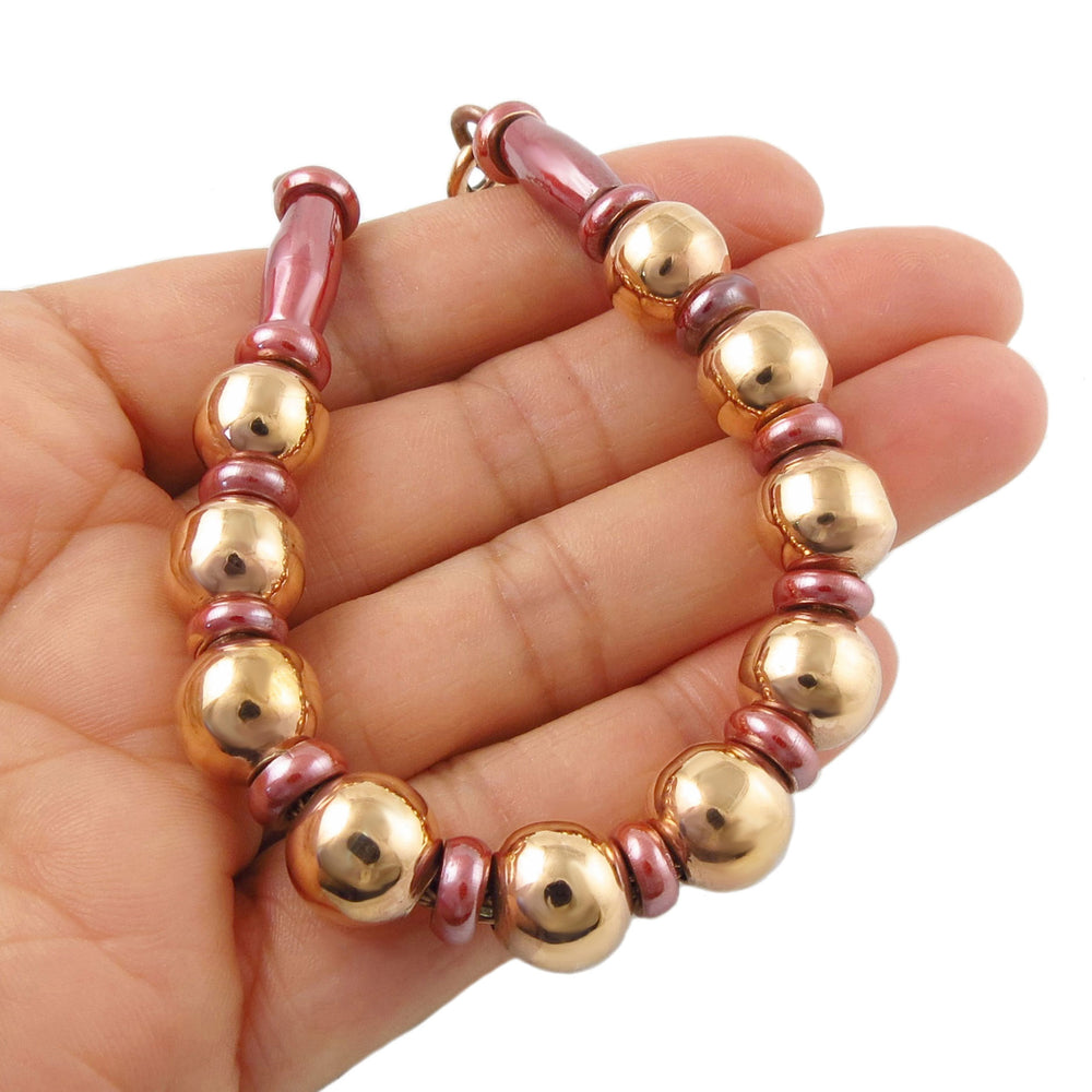 Women's bracelet with copper ball beads and pink spacers on a woman's hand against a white background