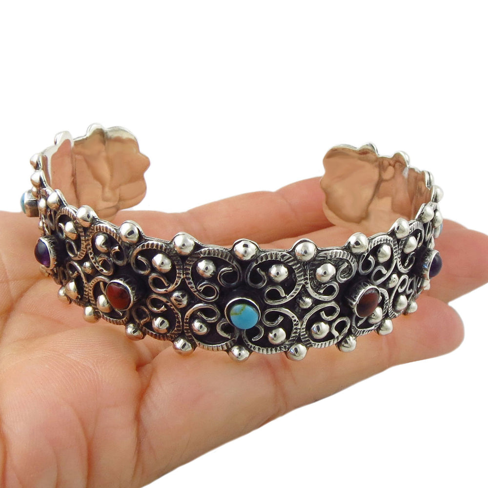 An ornate solid Mexican 925 sterling silver cuff bracelet with intricate filigree detailing and colourful gemstone accents, held in a person's hand against a plain white background.