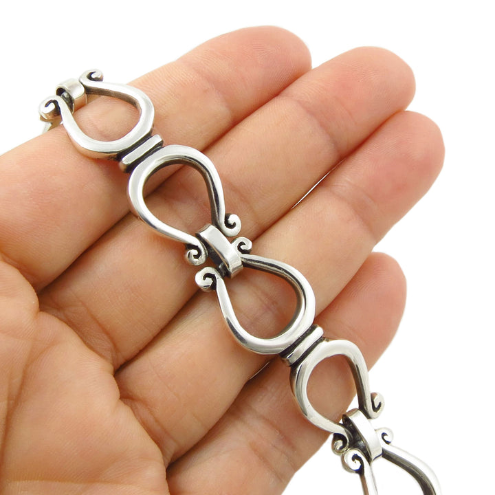 A close-up of a 925 sterling silver horseshoe link chain bracelet with ornate loop links, resting on a woman's hand against a white background.