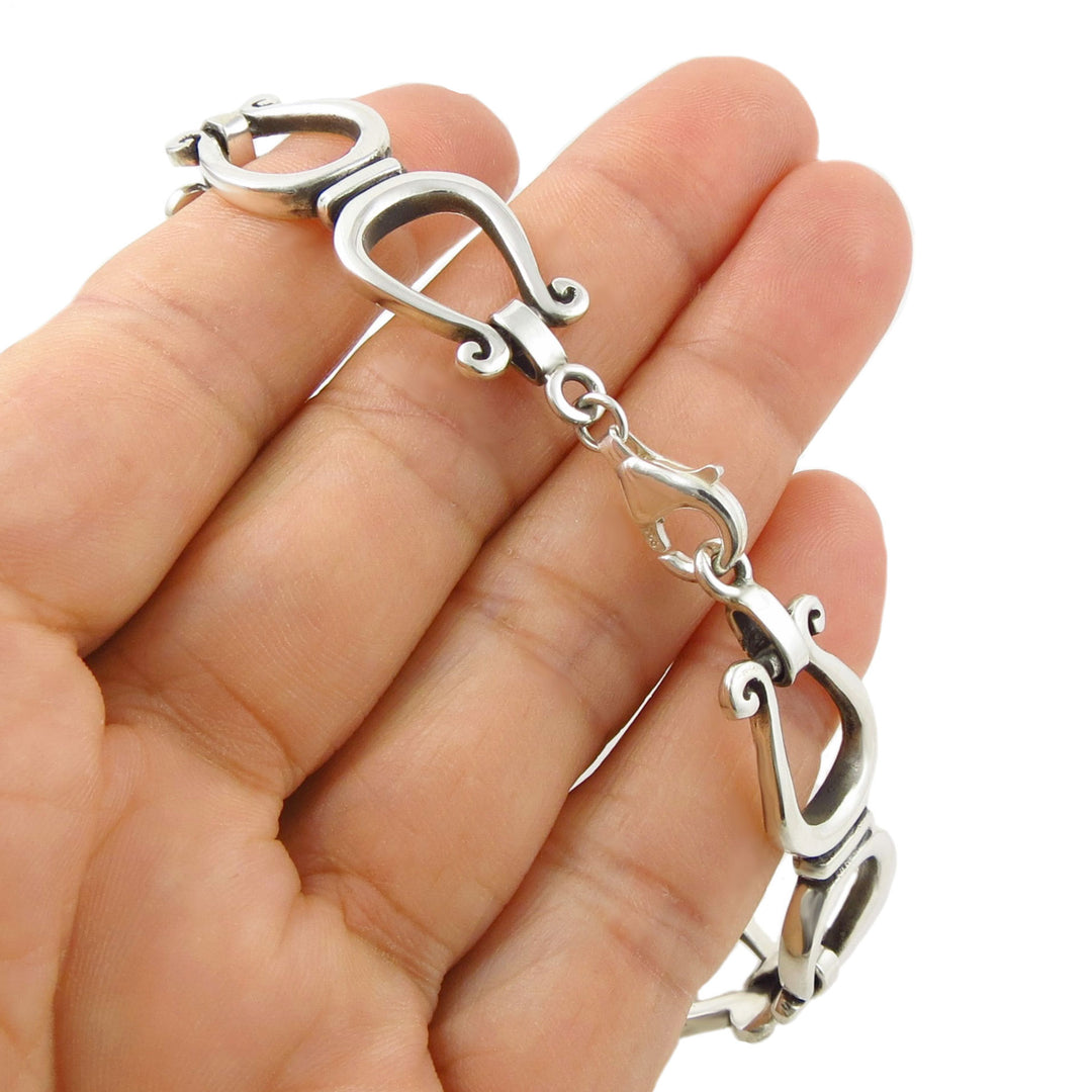 A close-up of a hand holding a 925 sterling silver horseshoe link bracelet with ornate interlocking links and a lobster clasp, against a plain white background.