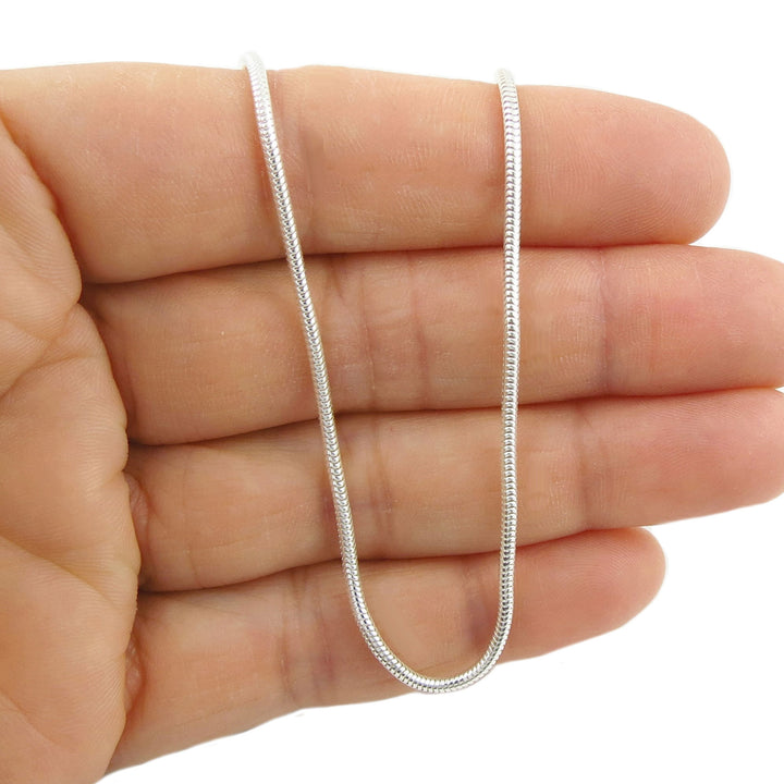 Silver snake chain held in a hand on a white background