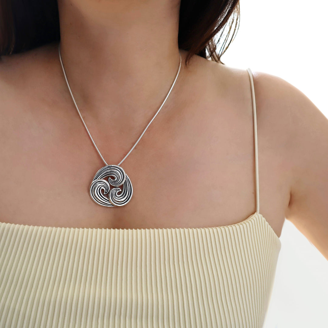 Silver snake chain necklace with a intricate pendant worn by a person in a beige top.