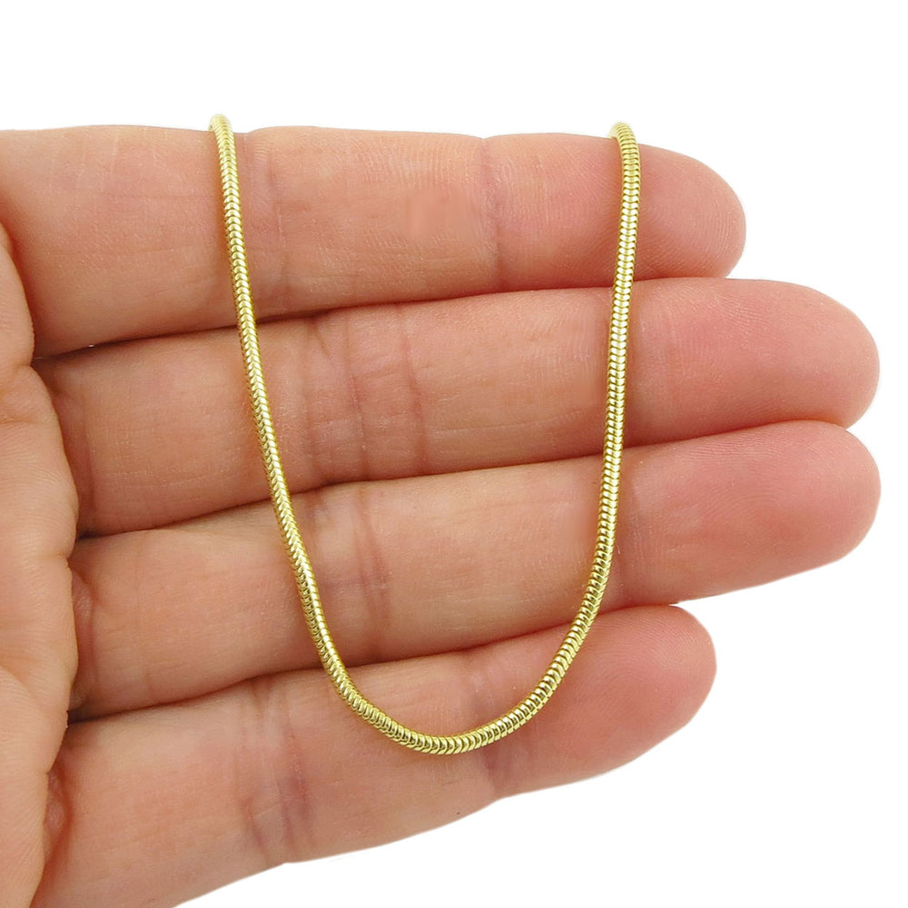Gold snake chain held between fingers on a white background