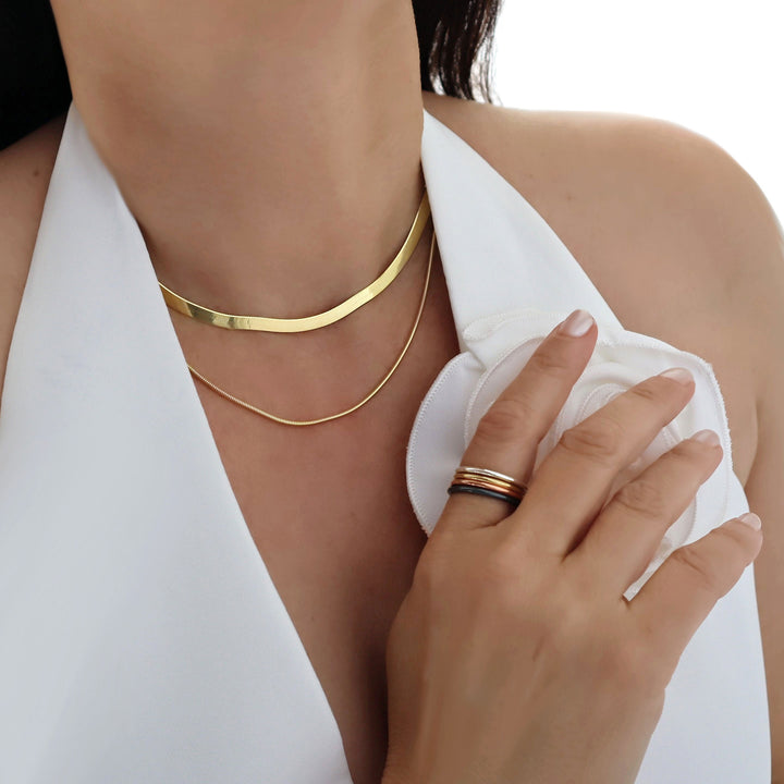 Gold necklace stack and rings on a person wearing a white top