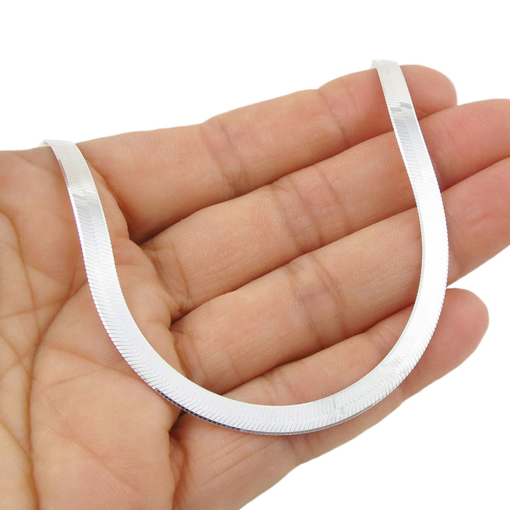 Flat silver snake chain necklace held in a hand against a white background