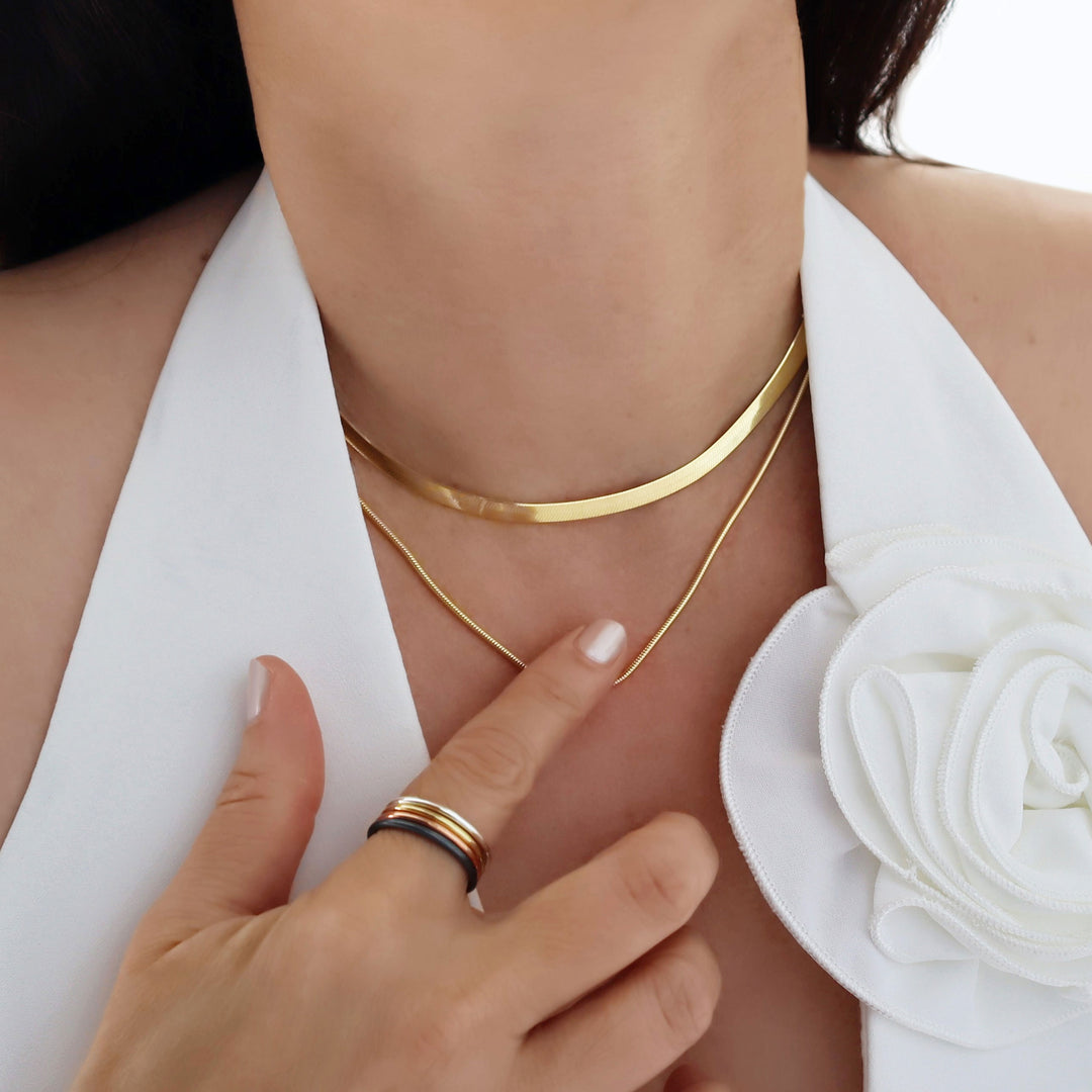 Gold necklace stack worn by a person with a white garment and floral detail.