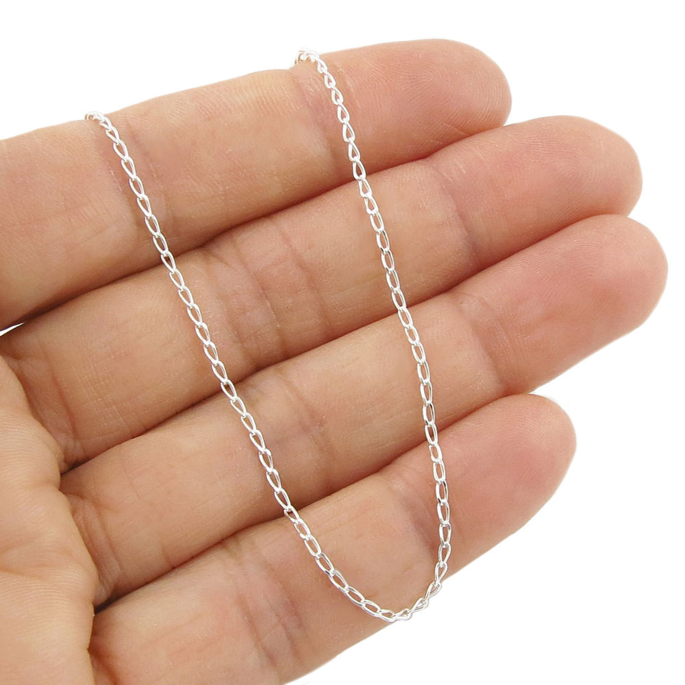 Silver curb chain held between fingers on a white background
