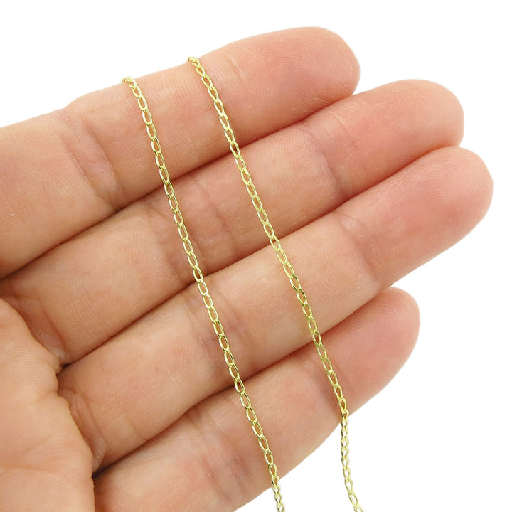 Yellow gold chain held between fingers on a white background