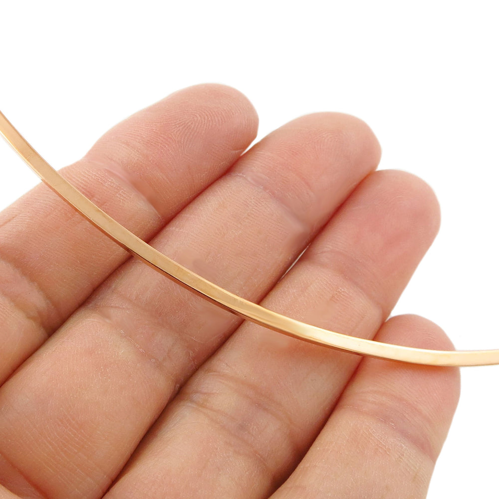 Copper choker necklace held between fingers against a white background