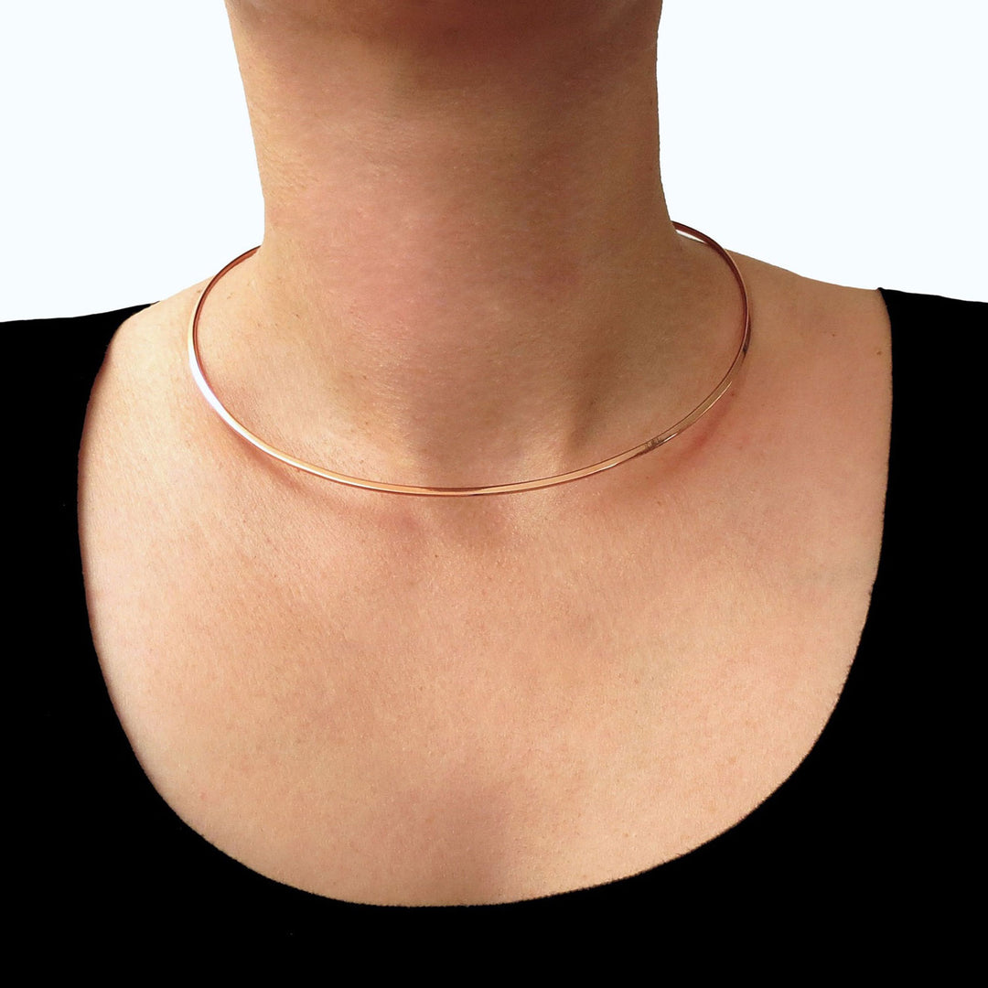 Large polished copper choker necklace torque worn by a woman on a white background