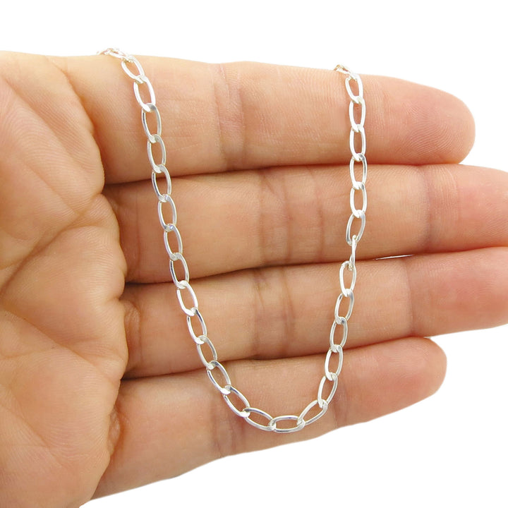 A silver paperclip chain necklace draped over a person's hand against a plain white background.