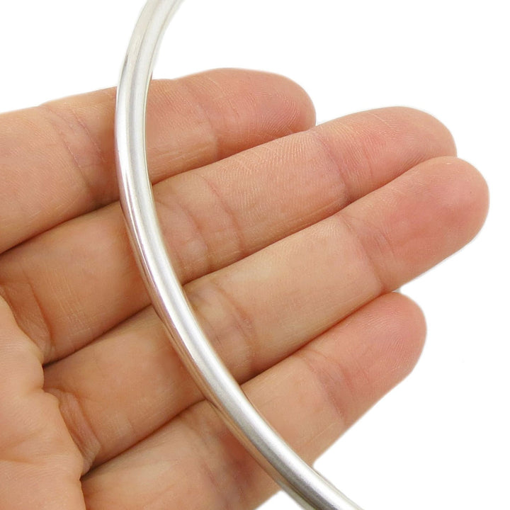 Silver slider tube choker held in a hand against a white background