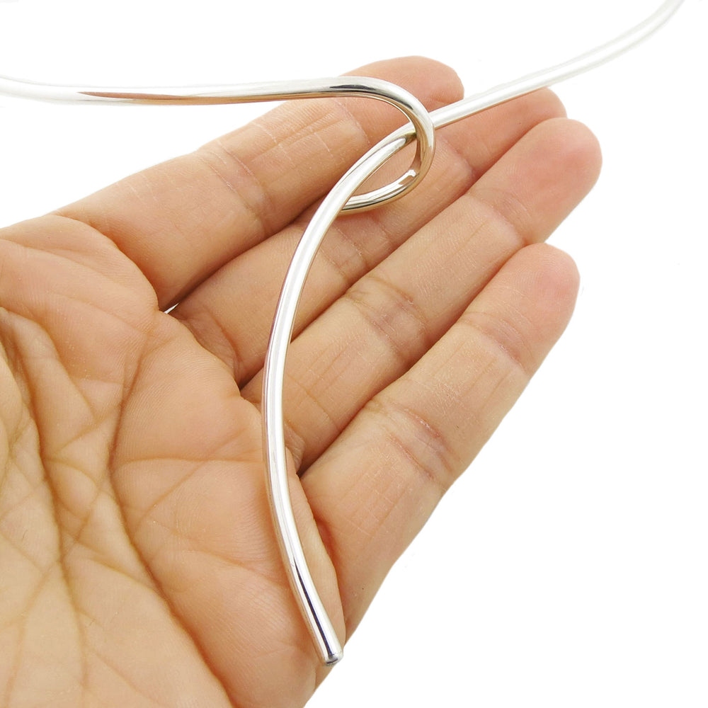 A silver choker toc necklace featuring a thin spiral tube held in a person's hand. 